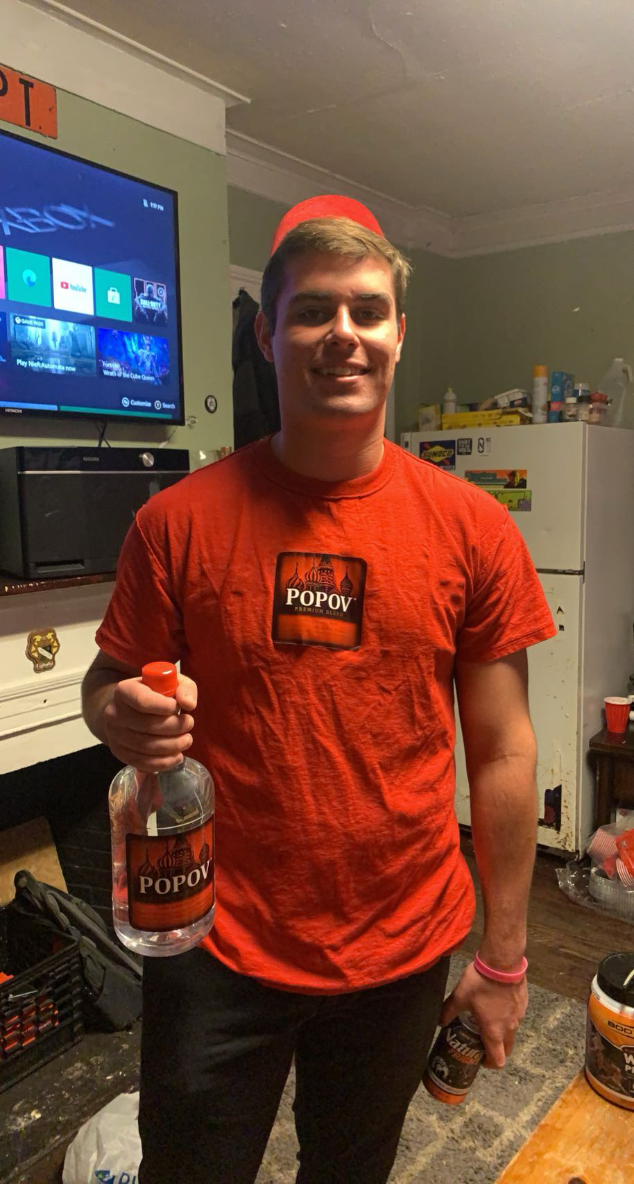 A man wearing a red Popov shirt and holding a Popov bottle